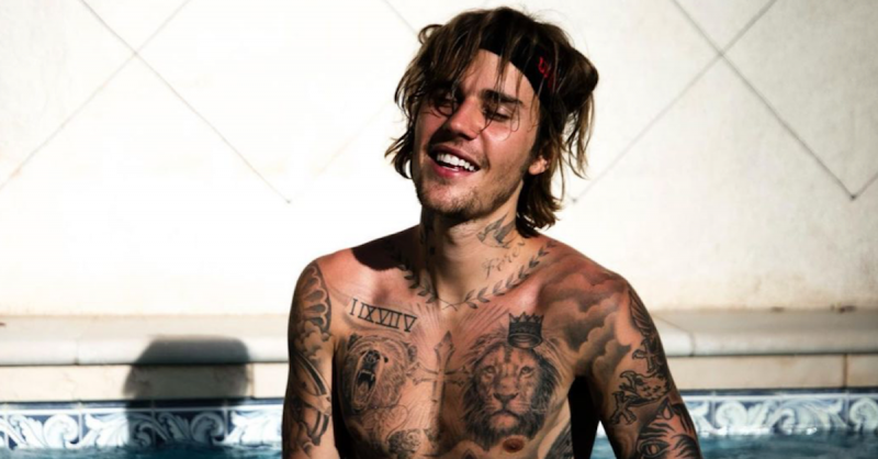   Justin Bieber lächelt mit nacktem Oberkörper, als er in einem Pool schwimmt und dabei seine vielen Tattoos enthüllt